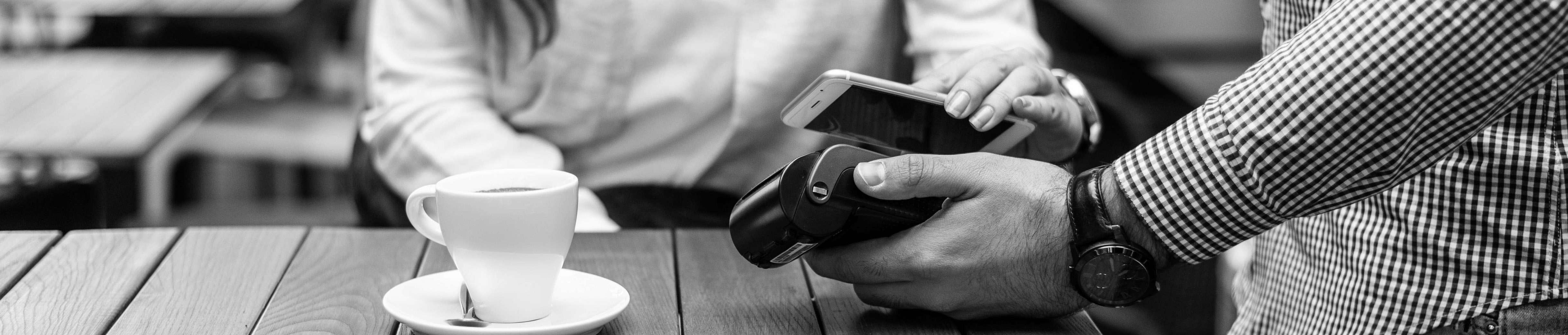 Individual utilizes contactless payment on their smartphone at coffee shop.