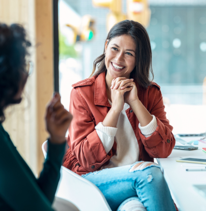 Woman smiling while sitting in chair listening to someone talk.