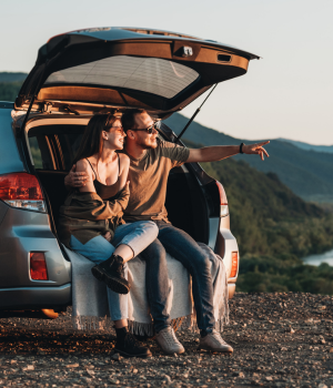Couple sitting on car trunk ledge looking at the sunset.