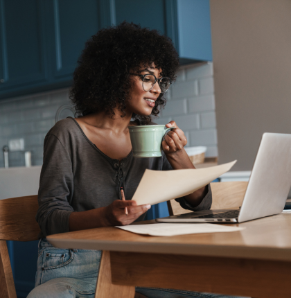 Woman holding coffee mug and looking at computer.