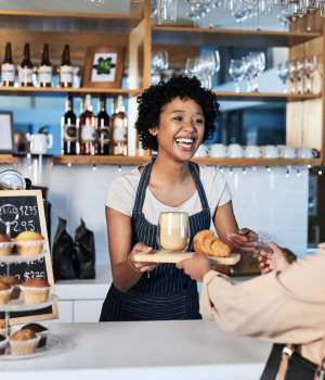 Happy coffee shop employee handing food and drink to customer.