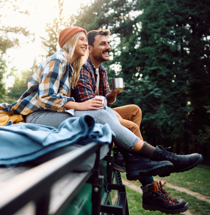 Couple enjoying nature while drinking coffee and sitting on vehicle.