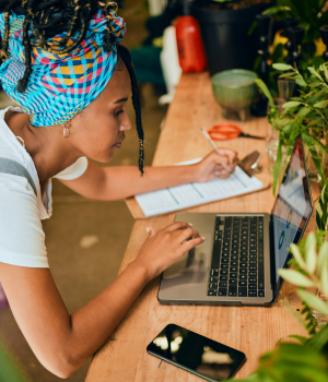 Business woman working on laptop and writing down information on clipboard.