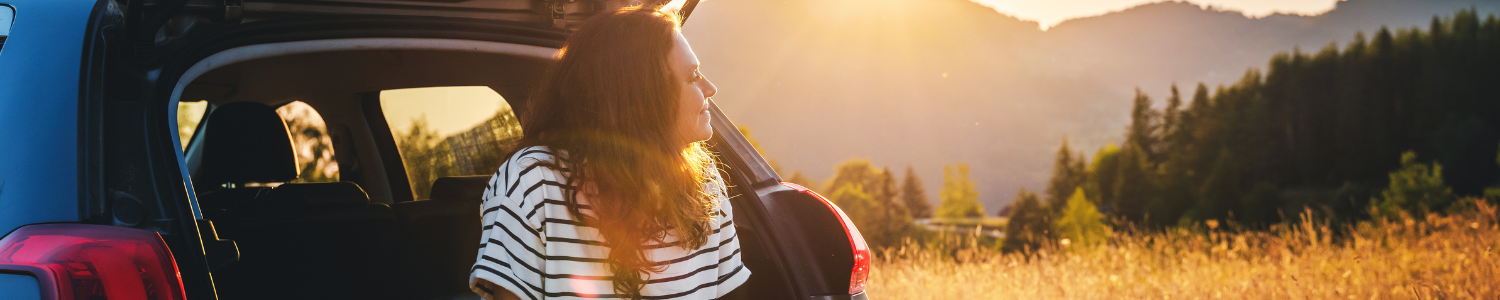Woman sitting on edge of car during mountain sunset.
