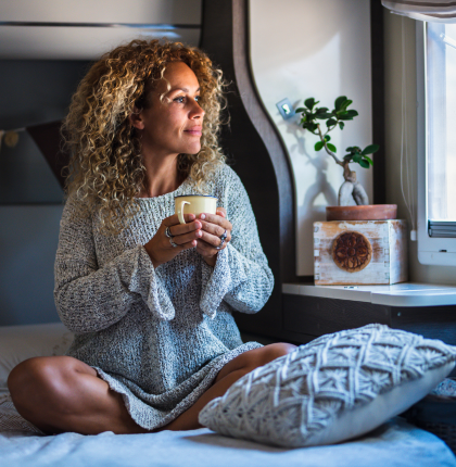 Woman holding coffee mug while sitting on bed.