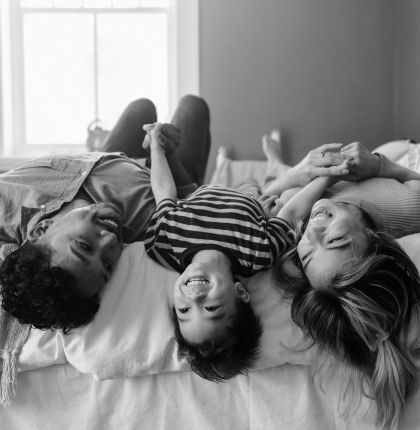 Family laying upside down on bed laughing together.