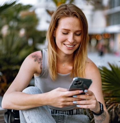 Woman smiling looking at phone while sitting outside.