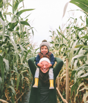 Son sitting on top of Mother's shoulders going through corn field.