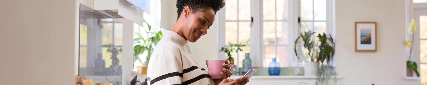 Woman on phone holding coffee in kitchen.