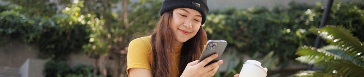 Woman sitting in park with coffee cup looking at phone.