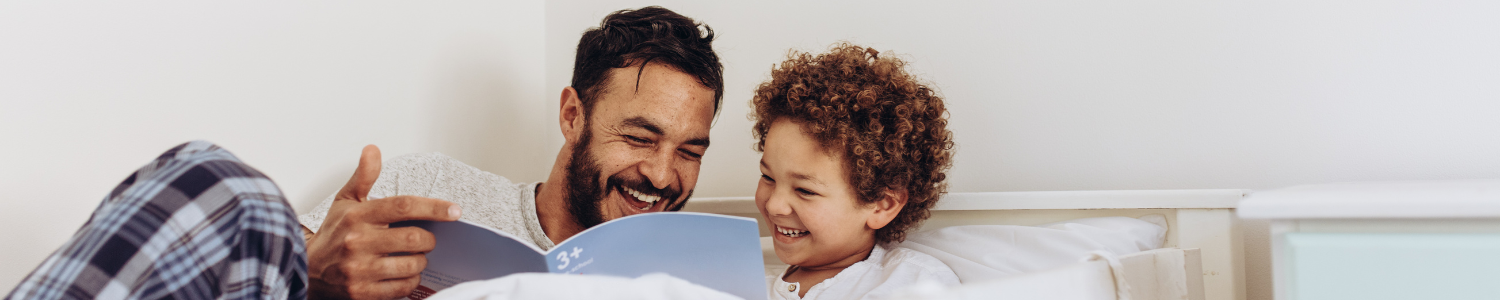 Father and Son reading in bed smiling.