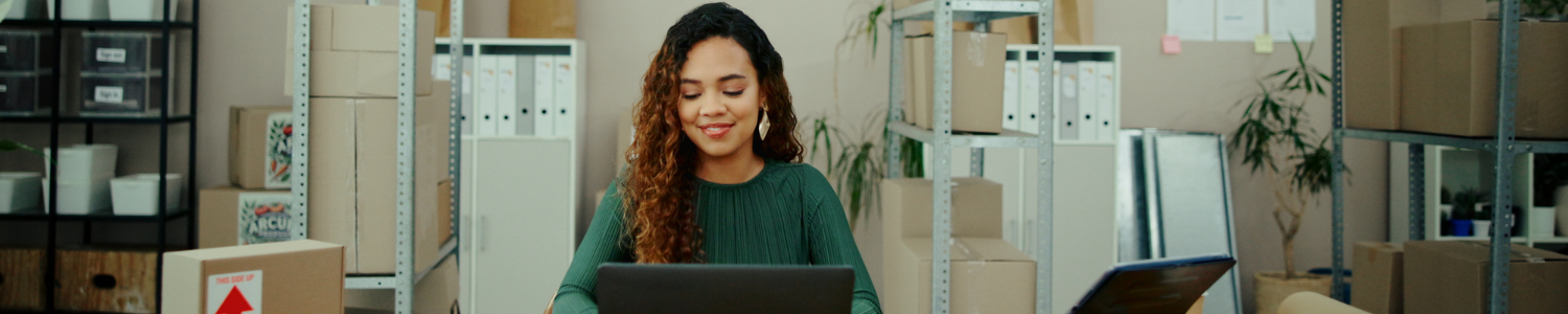 Woman working on computer surrounded by boxes and office supplies.